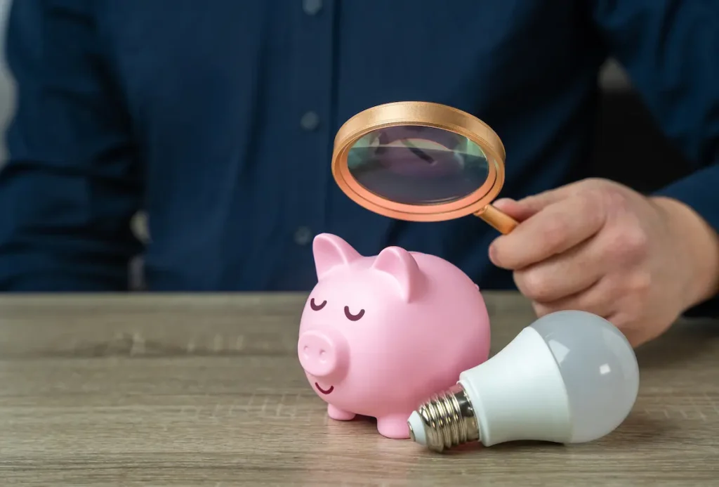 Man looking at a piggy bank and lightbulb with a magnifying glass
